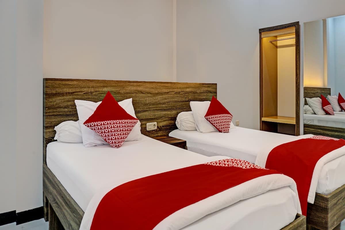 Ein Hotelzimmer mit zwei Betten, jeweils mit weißer Bettwäsche und roten Akzenten, Holz-Kopfteilen und einem großen Spiegel an der Wand.