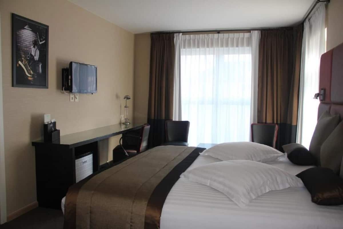 A hotel room with a bed, a desk, a chair, a television, and a window with curtains.