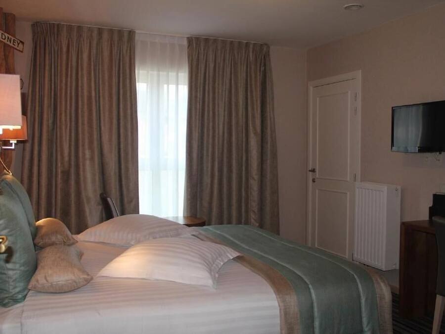 A hotel room with a bed, curtains, a television, and a sign that reads "SYDNEY".