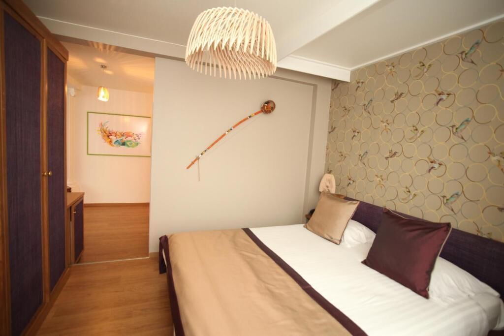 A bedroom with a bed, a hanging light fixture, a wall-mounted clock, and a door leading to another room.