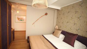 A bedroom with a bed, a hanging light fixture, a wall-mounted clock, and a door leading to another room.