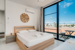 Un dormitorio moderno con una cama grande, una mesita de noche con lámpara, un adorno de pared y vistas de la ciudad a través de amplios ventanales.