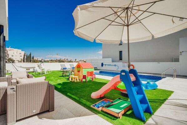 Un área de piscina en la azotea con tobogán, zona de juegos infantiles y mobiliario exterior.