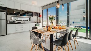 Une cuisine moderne avec des meubles blancs, un coin repas doté d’une table en bois et de chaises noires, et une grande fenêtre offrant une vue sur l’extérieur.