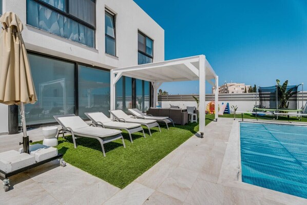 Un área de piscina en la azotea con sillones de descanso, una pérgola y vistas de la ciudad.