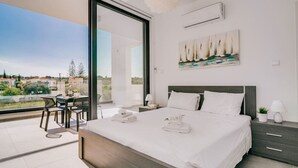 A modern bedroom with a large bed, a painting of sailboats, and a balcony with a table and chairs. - SunnyVillas:2BR+Ensuite CozyVilla*Private Pool*AL9 (Paralimni)