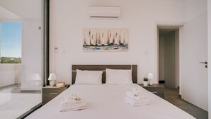 A modern hotel room with a large bed, a painting of sailboats, and a view through a glass door. - SunnyVillas:2BR+Ensuite CozyVilla*Private Pool*AL9 (Paralimni)