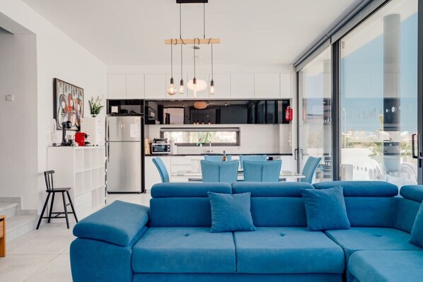 Una cocina moderna con armarios blancos, horno integrado y zona de comedor con sillas azules.