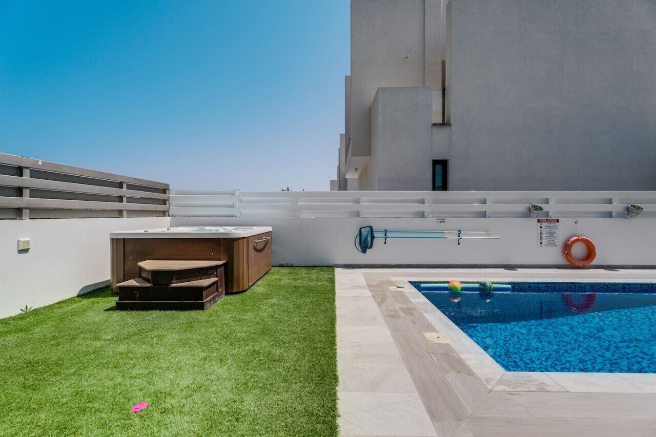 A rooftop pool area with a hot tub, a small seating area, and a clear blue pool.