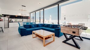 Ein modernes Wohnzimmer mit einem blauen Ecksofa, einem Holztisch und einem Kicker.