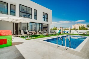 Un edificio moderno con piscina, asientos exteriores y vistas a otros edificios.