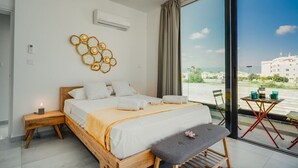 Ein Schlafzimmer mit einem großen Bett, einem Nachttisch, einem kleinen Tisch mit Getränken und Blick ins Freie.