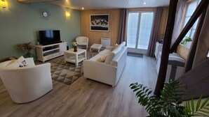 A living room with a sofa, armchair, TV, and a painting on the wall. - Charming Cottage in Taintrux: Hiking, Skiing, Close to Saint-Dié & Alsace Attractions (Taintrux)