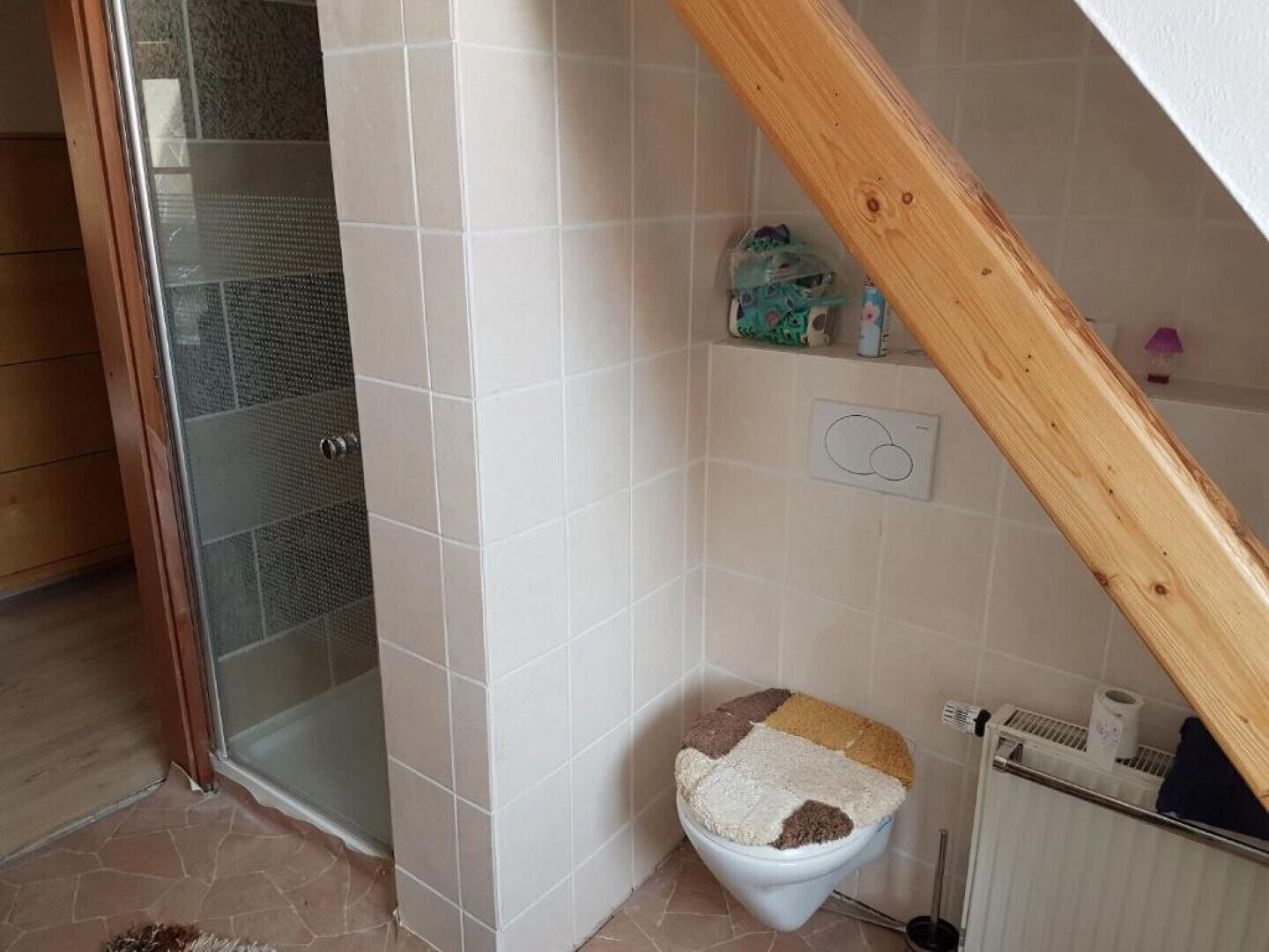 Un baño pequeño con ducha, un inodoro con asiento acolchado y un radiador.