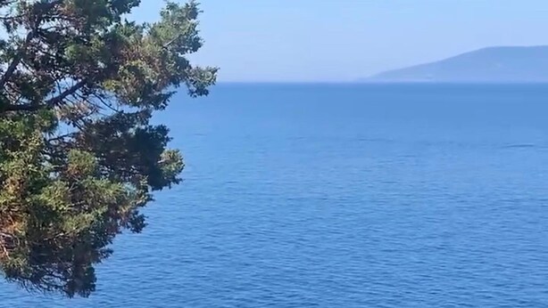 Ein Poolbereich mit einer Steindeck, blauen Sonnenschirmen und Blick auf das Meer.