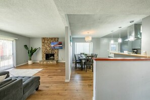 A modern living room with a stone fireplace, a dining area with a wooden table, and a kitchen with a white countertop. - Cozy, Calm, Cool 3Bd fenced yard (Monrovia)