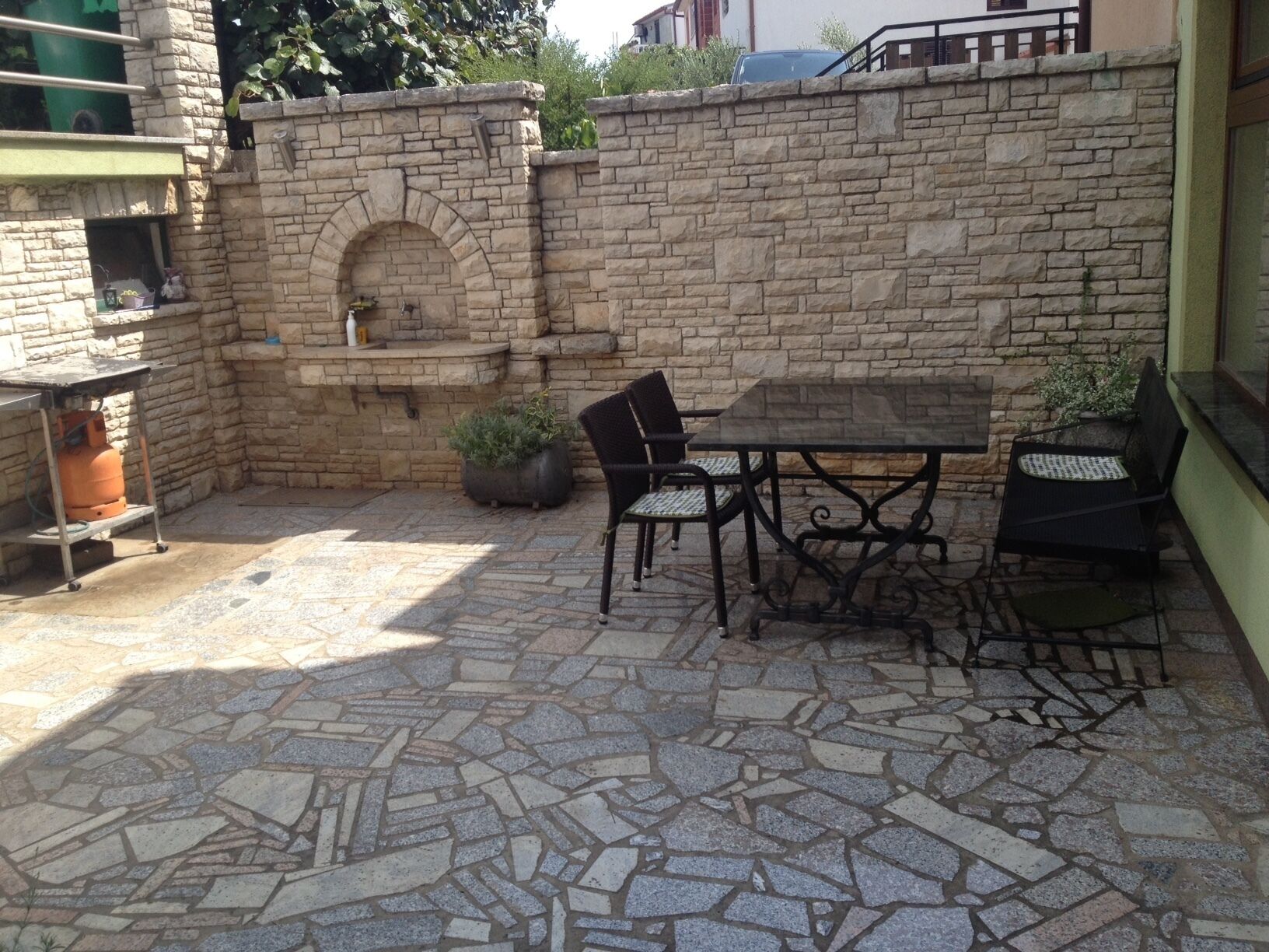 A stone patio with a table and chairs, a brick oven, and a gas tank.