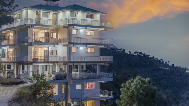 A multi-story building with balconies, a covered upper level, and a view of a hilly landscape. - The Mountains Retreat (Krishangarh)