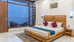 A bedroom with a wooden bed, a view to the outside, a small bedside table, and a wall-mounted light. - The Mountains Retreat (Krishangarh)