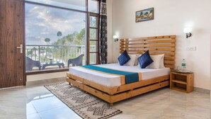 A bedroom with a wooden bed, a view of the outdoors, and a balcony with chairs. - The Mountains Retreat (Krishangarh)