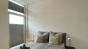 Ein Schlafzimmer mit einem Bett, Kissen, einer Nachttischlampe und einem Fenster mit Jalousien.