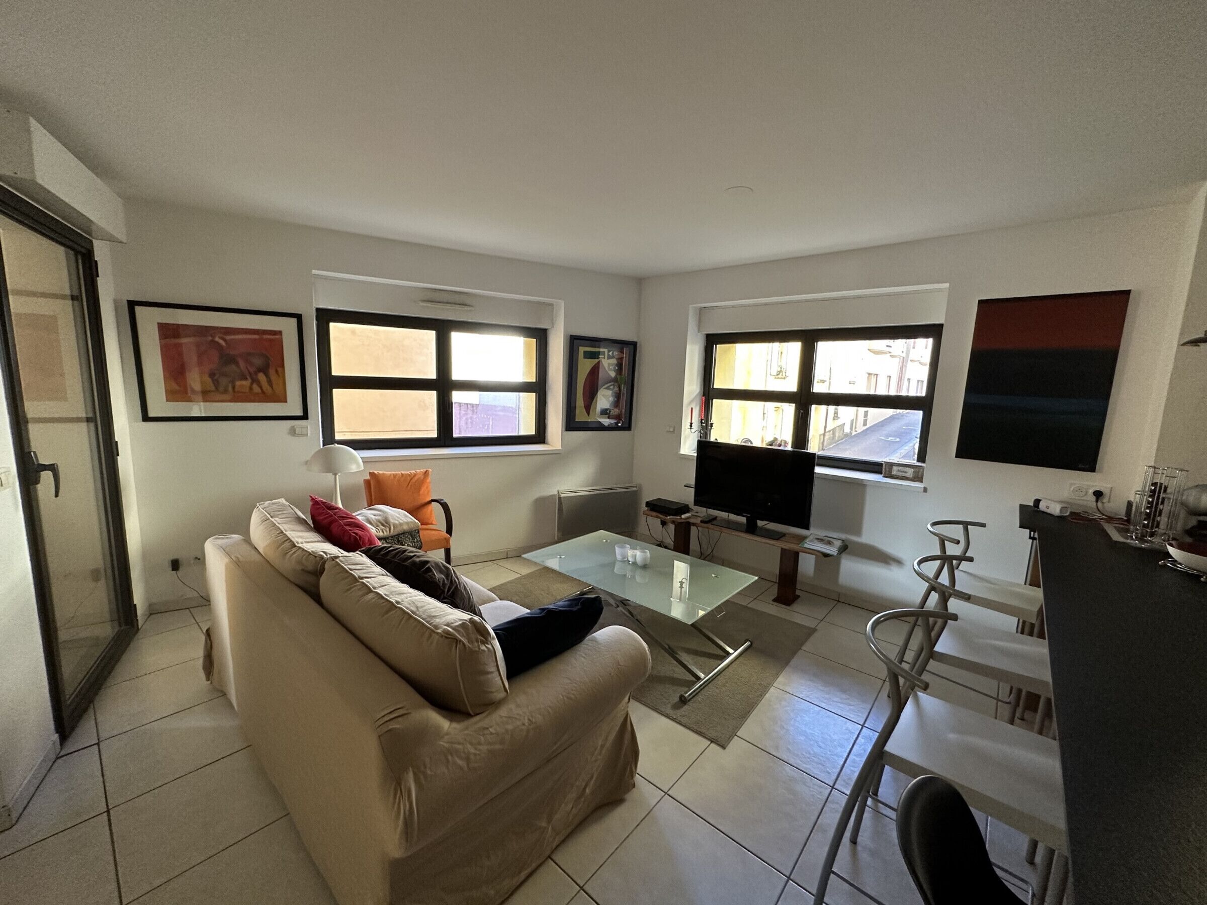 A living room with a sofa, a glass coffee table, a TV, and a dining area with a bar.