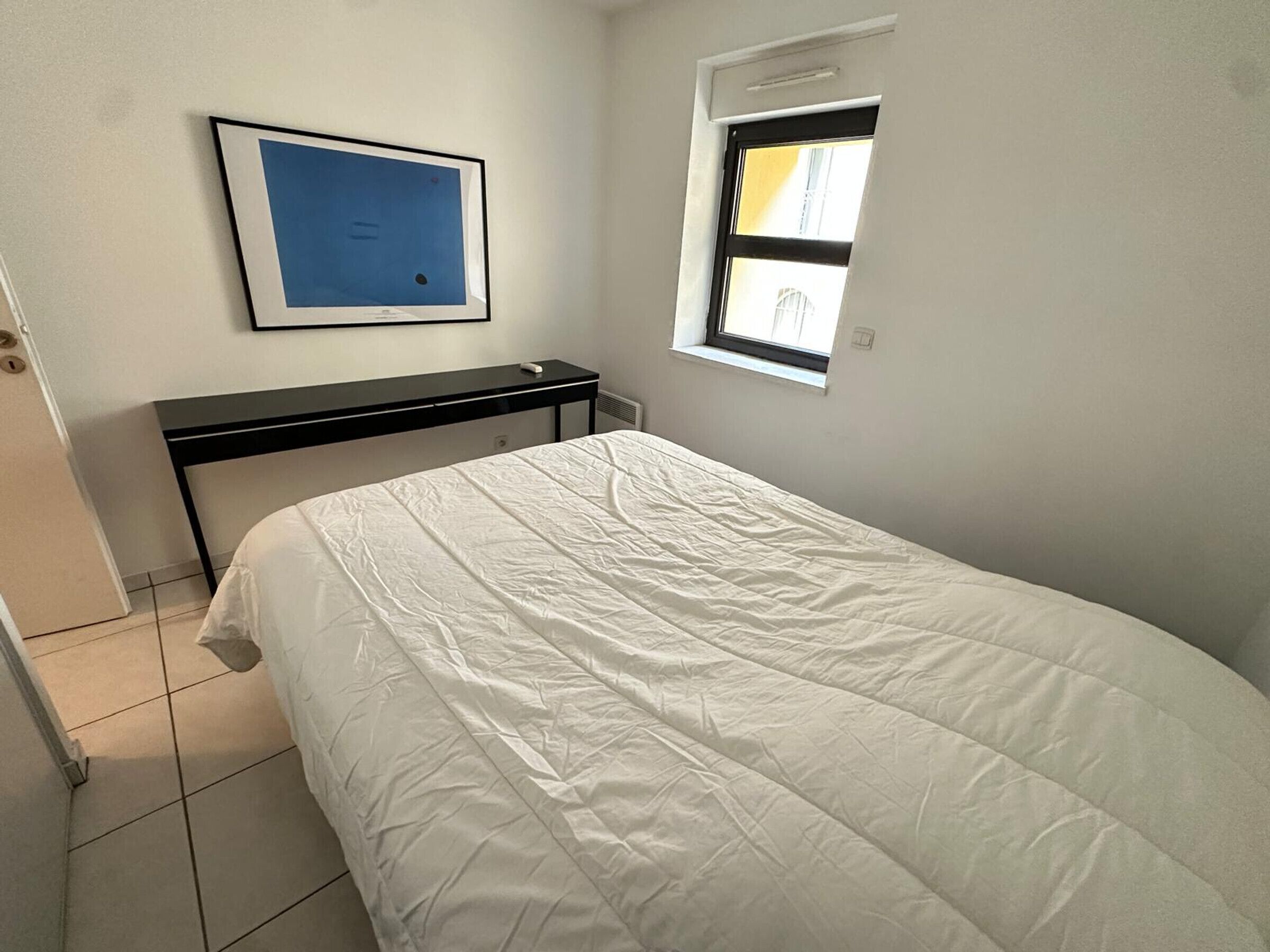Une petite chambre à coucher, bien rangée, avec un lit, un bureau et une fenêtre.