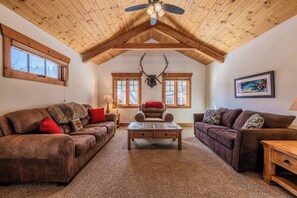 A cozy living room with two leather sofas, a wooden coffee table, and a ceiling fan.