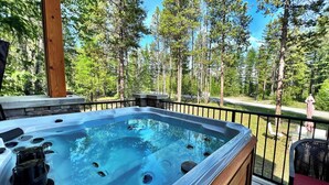 Un jacuzzi en una terraza de madera con borde de piedra, rodeado por una barandilla de metal y árboles.