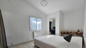 A bedroom with a bed, a bedside table, a lamp, a window, a radiator, and a mirror.