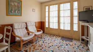 A room with two wooden chairs, a television, and a large window with curtains.