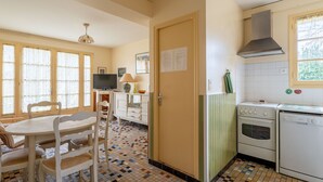 A compact kitchen with a tiled floor, a dining area with a table and chairs, a television, and a stove.