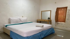 Una cama bien hecha con ropa de cama blanca y azul, una mesita de noche de madera con un espejo y una ventana con cortina marrón.