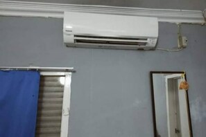 A room with a white air conditioning unit mounted on the wall, a window with a blue curtain, and a door with a hanging ornament. - Super OYO 90483 Homestay Permata (Bangko)