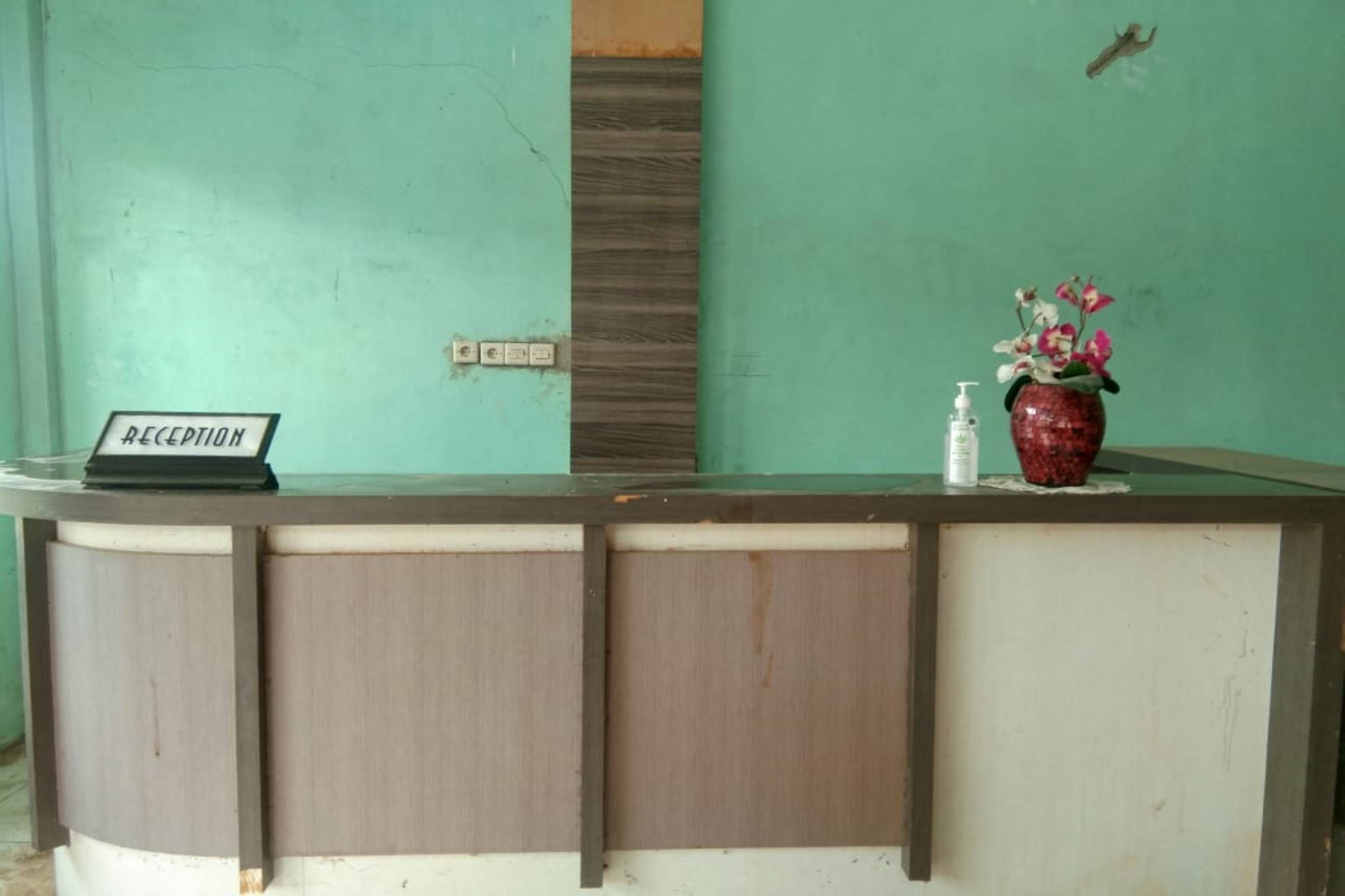 A reception desk with a sign, a vase with flowers, and a hand sanitizer bottle.