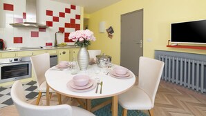 Un comedor con una mesa redonda dispuesta para cuatro personas, rodeada de sillas blancas. Un jarrón con flores rosas está sobre la mesa.