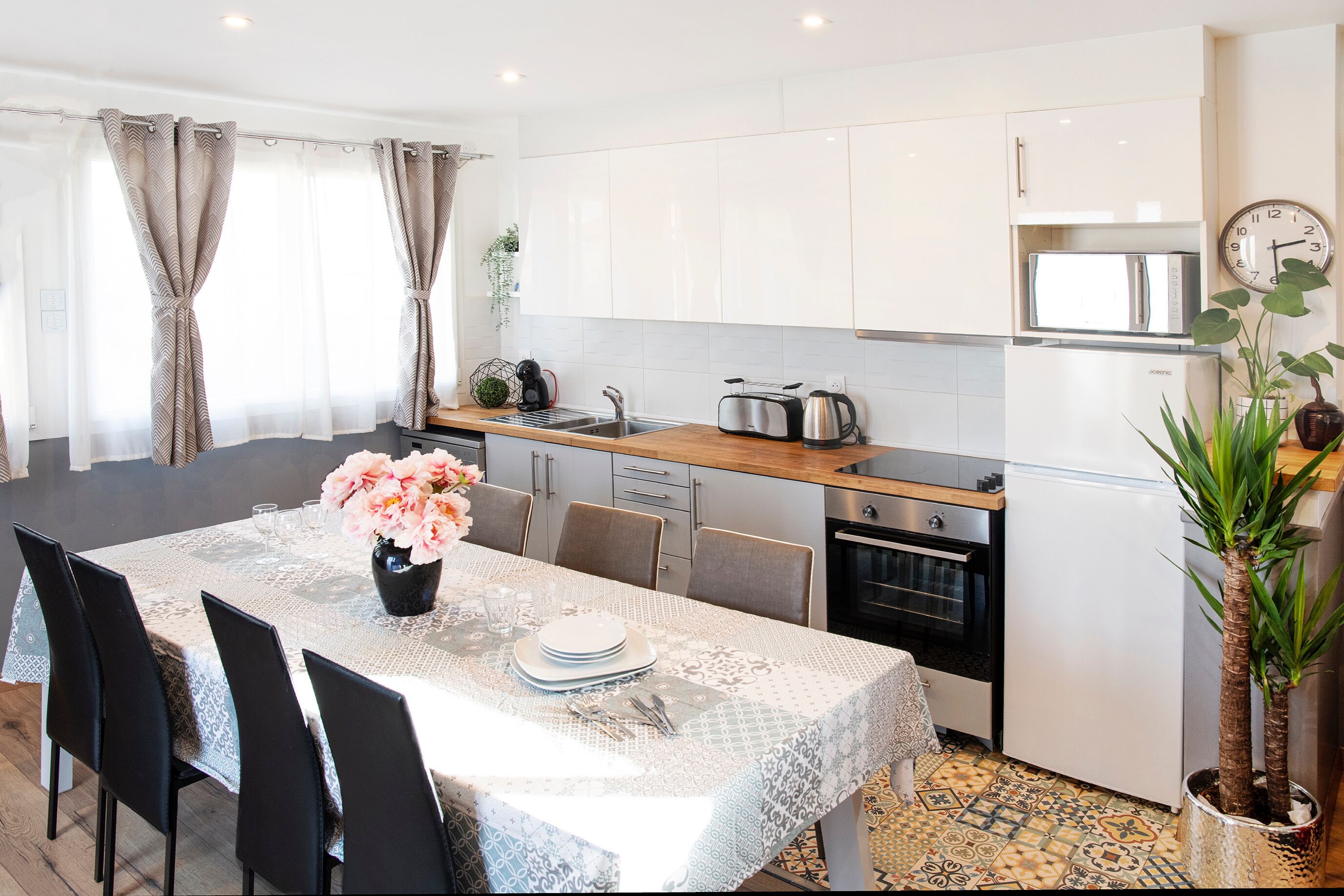 A modern kitchen with white cabinets, a wooden countertop, and a dining area with a lace tablecloth.