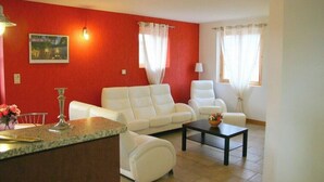 Una sala de estar con una pared roja, sofás blancos, una mesa de centro y un cuadro.
