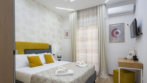 A modern hotel room with a large bed, a bedside table, a TV, and a window with curtains. - MarGab Guest House Yellow Room (Napoli)