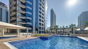 Piscina con sillas de descanso, rodeada de edificios modernos y palmeras.