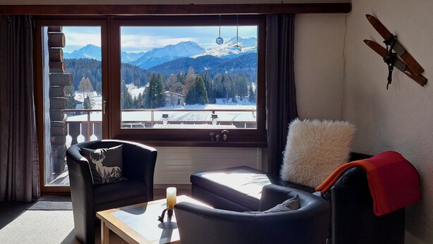 A cozy room with a large window offering a mountain view, a wooden ceiling, and a rustic decor including a wooden wall hanging. - Stgirat Bellaval by Interhome (Valbella)