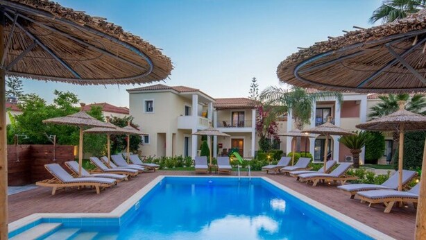 A swimming pool with lounge chairs and umbrellas, surrounded by buildings with balconies.