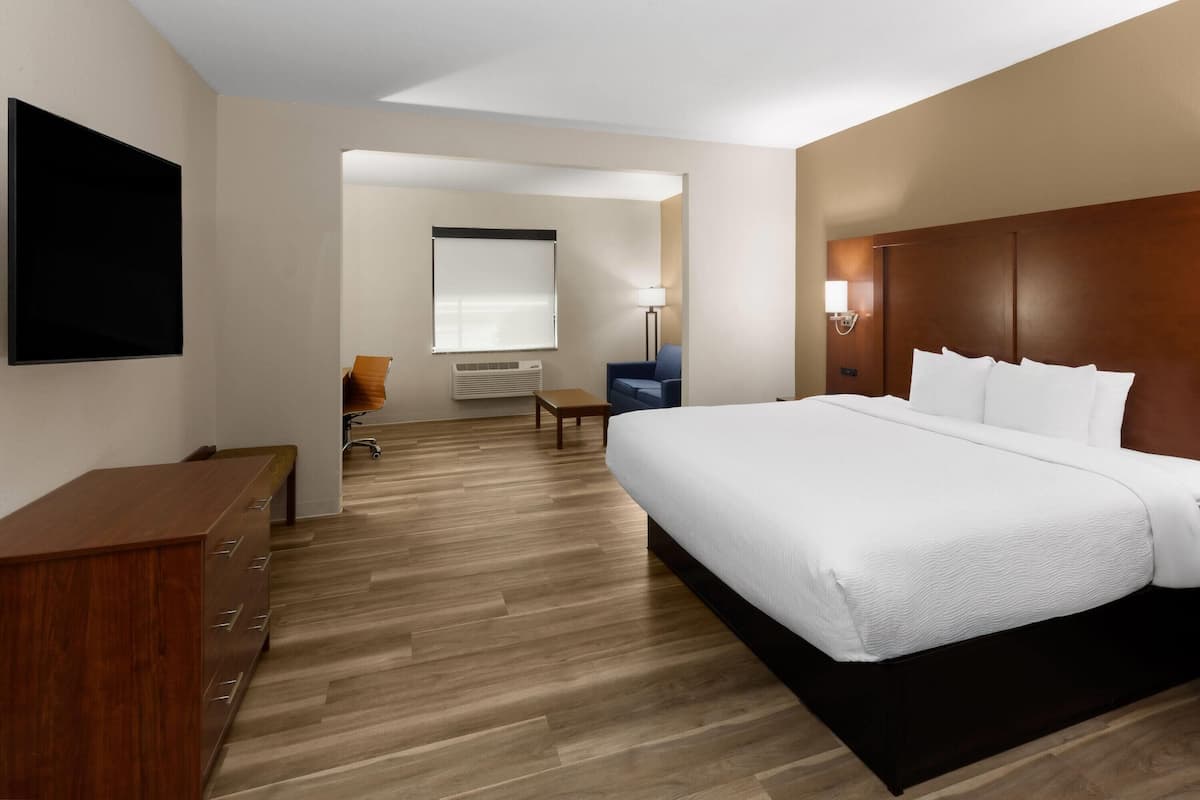 Ein Hotelzimmer mit einem großen Bett, einem Schreibtisch mit Schubladen, einem Stuhl, einer Lampe und einem Fernseher an der Wand.