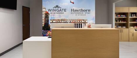 A hotel reception area with a wooden reception desk, a Dell computer, and a large poster advertising 'Wingate by Wyndham' and 'Hawthorn Extended Stay by Wyndham'.
