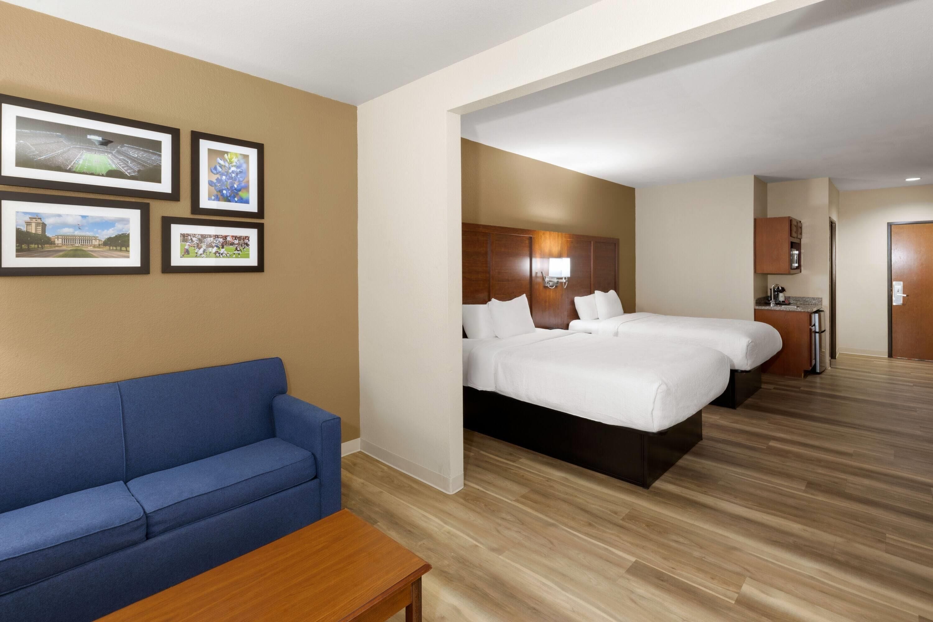 Une chambre d’hôtel avec un grand lit, un canapé bleu, une table en bois et des tableaux encadrés au mur.