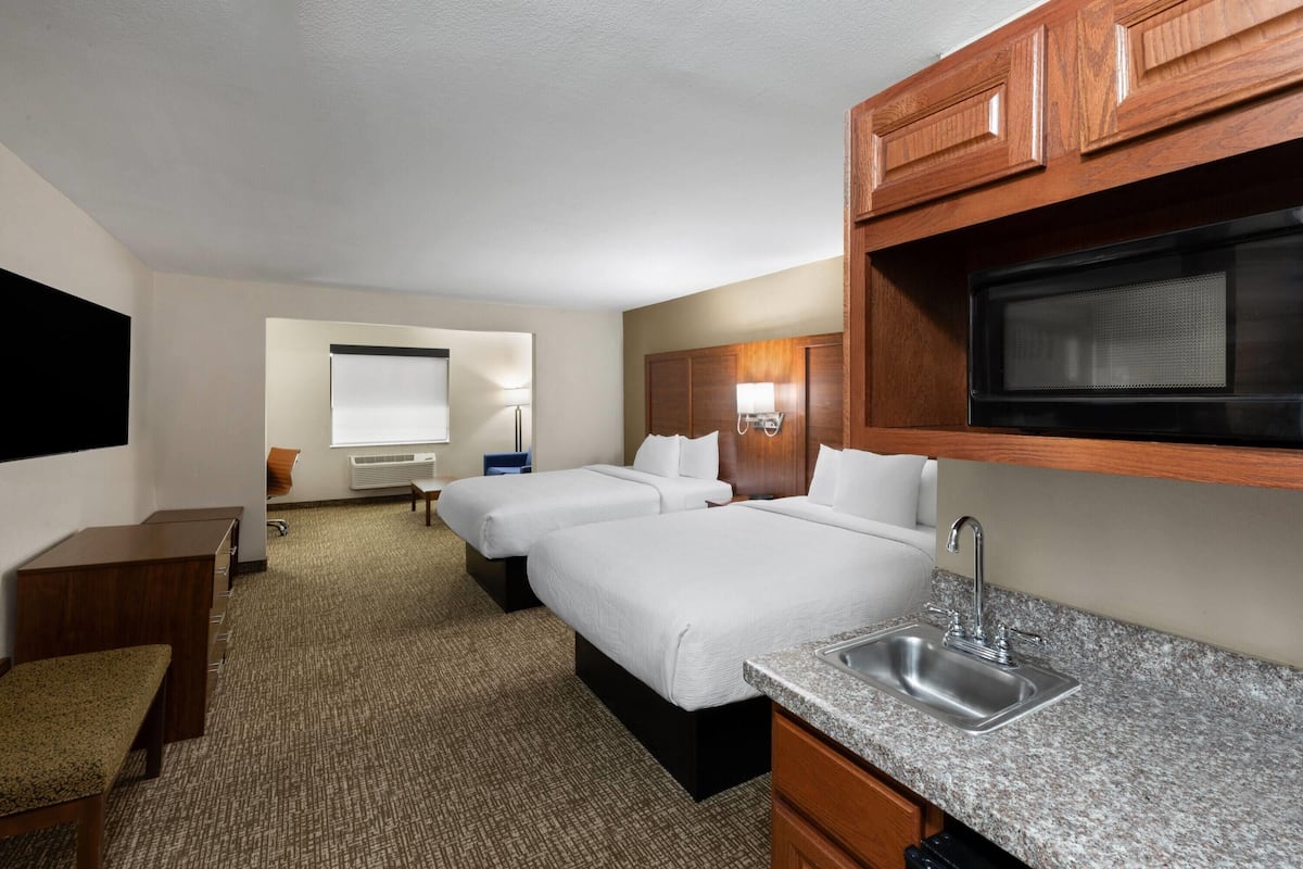 Ein Hotelzimmer mit zwei Betten, einer Küchenzeile mit Mikrowelle, einem Waschbecken und einem kleinen Schreibtisch.