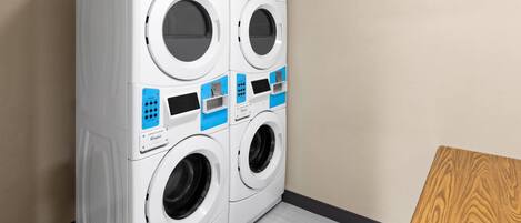 Un appareil combiné lave-linge et sèche-linge à chargement frontal, doté de quatre portes et de panneaux de commande, situé dans une pièce dont le sol est recouvert de parquet clair et dont un des murs est de couleur unie.