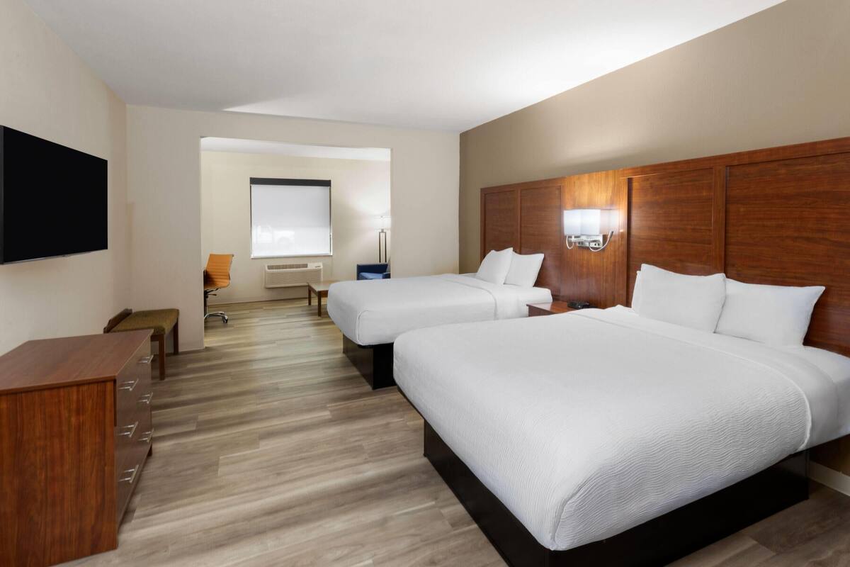 Ein Hotelzimmer mit zwei Betten, einem Holzkopfteil, einem Flachbildfernseher, einem Schreibtisch und einem Stuhl.