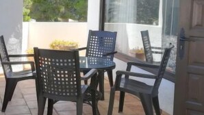 A patio with a table and chairs, a window with a view of trees, and a door. - Toscamar by Interhome (Jávea)