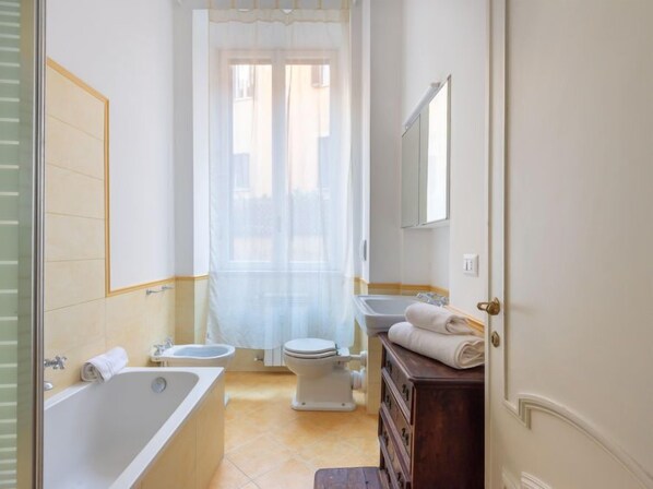 A bathroom with a bathtub, toilet, bidet, and a wooden dresser with towels. - Virgilio by Interhome (Roma: Piazza Navona - Campo dei Fiori)